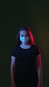 Click fingers. Pandemic restriction. Woman in protective mask blue red neon light glow snapping. Looking at camera isolated on black vertical copy space. New normal. Advertising information