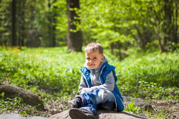 Portrait of a boy in a blue tank top in the woods in spring. Take a walk in the green park in the fresh air. The magical light from the sun's rays falls behind the boy.