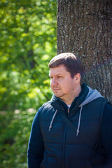 Portrait of a man at a tree in the forest in spring. Take a walk in the green park in the fresh air. The magical light from the sun's rays was left behind. Space for copying. Selective focus.