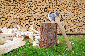Split logs, an axe on a block on the background of a pile of chopped firewood in the yard of a...