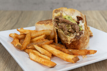Appetizing carne asada steak burrito cut in half and served with french fries for a tempting Mexican food delicacy