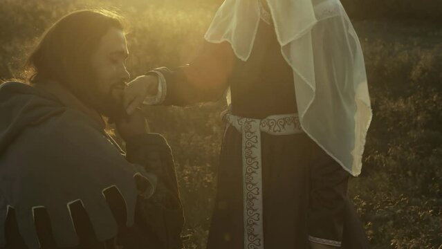 Portrait of a medieval warrior who kisses the hand of his beautiful medieval young woman in the bright rays of the sunset