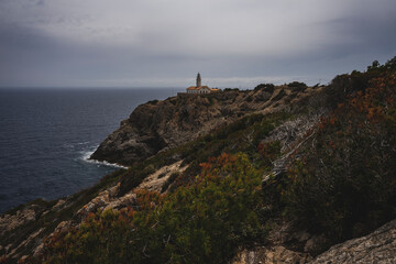 Fototapeta na wymiar Biała latarnia morska na skalistym klifie w pochmurny dzień. Latarnia położona jest na wschodnim wybrzeżu Majorki. 