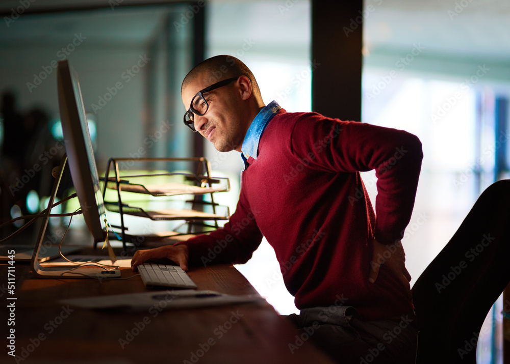 Canvas Prints Sitting for too long can have adverse effects. Shot of a young man holding his back in pain while working late in the office.