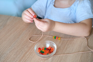 small child, toddler stringing colored plastic beads on string, kid's fingers close-up, concept of...