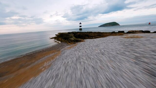 FPV Aerial view of penmon point light house, fast low flying towards the light house then around showing the landscape area. birds eye view North Wales UK