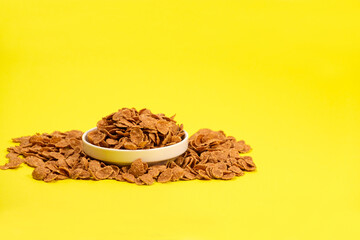 Durum wheat flakes - quick breakfast cereal on a plate on a yellow background, space for text.