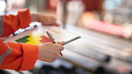 A worker is holding luxury pen and assessment paper form, preparing to do project evaluation, with blurred background of factory place. Industrial working scene action photo. Selective focus. - obrazy, fototapety, plakaty