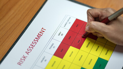 Action of a person is using ballpoint pen to marking on the risk assessment matrix table at 