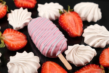 Pink ice cream on a stick, meringue and strawberries on a black background.