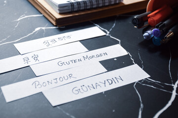 Good morning greetings in different languages ​​on white pieces of paper on study table. Educational teaching concept, Selective focus. © Debalina