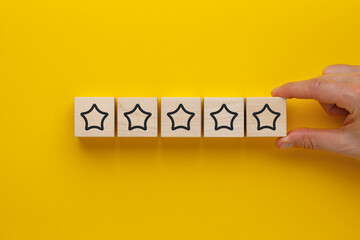 Wooden cubes with five stars on a yellow background. Concept of service rating and evaluation.