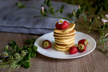 Foodphoto. Pancakes with strawberries close-up. decorated with flowers. The composition is complemented by leaves and greens in a basket. Picnic or summer breakfast.