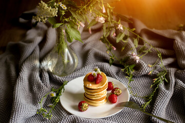 Foodphoto. Pancakes with strawberries close-up. decorated with flowers. The composition is complemented by leaves and greens in a basket. Picnic or summer breakfast.
