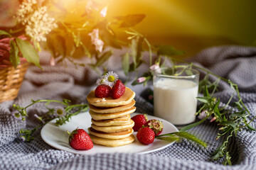 Foodphoto. Pancakes with strawberries close-up. decorated with flowers. The composition is complemented by leaves and greens in a basket. Picnic or summer breakfast.