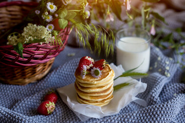 Foodphoto. Pancakes with strawberries close-up. decorated with flowers. The composition is complemented by leaves and greens in a basket. Picnic or summer breakfast.