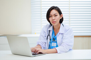 Working on laptop. Female asian doctor sitting on desk office at modern medical center. Healthcare medical and medicine concept.