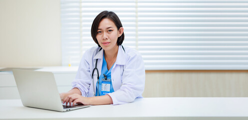 Working on laptop. Female asian doctor sitting on desk office at modern medical center. Healthcare medical and medicine concept.