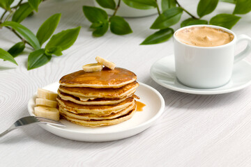 a stack of delicious pancakes with syrup, bananas and a cup of aromatic coffee
