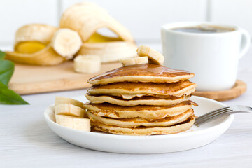 a stack of delicious pancakes with syrup, bananas and a cup of aromatic coffee