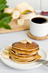 a stack of delicious pancakes with syrup, bananas and a cup of aromatic coffee