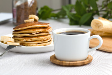a cup of black coffee on the background of a stack of pancakes with bananas