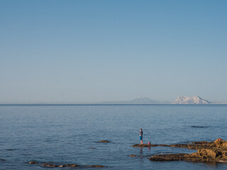 Man fishing in the Mediterranean Sea and with a blue sky with the Rock of Gibraltar and the Altas Mountain (Africa) in the background. You see another continent