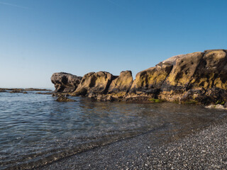 Fototapeta na wymiar Small stone beach shore in the mediterranean sea on the Costa del Sol. Transparent water and eroded rocks in Manilva