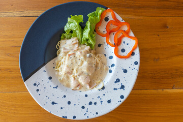 Spaghetti Carbonara Made from spaghetti with ham and vegetables Topped with Carbonara Sauce was put in a blue and white plate.