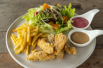 Battered fish steak on a white plate was salad and salad dressing on the side of the dish. on the wooden table.
