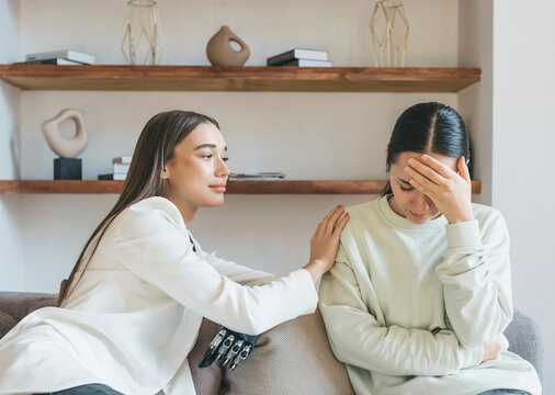Two beautiful young European women, one with a bionic prosthesis on her arm, are sitting on the couch, experiencing stress, being depressed. Emotional support, burnout