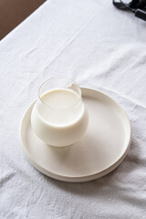 A glass of milk on a light plate on a table with a white tablecloth