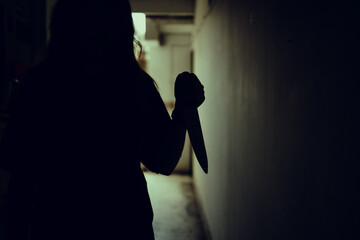 The shadow of a female murderer stood terrifyingly holding a knife and lit from behind.Scary horror...