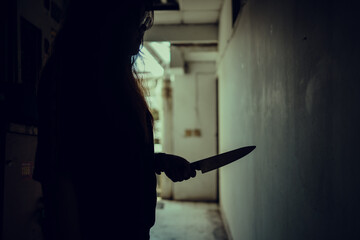 The shadow of a female murderer stood terrifyingly holding a knife and lit from behind.Scary horror or thriller movie mood or nightmare at night Murder or homicide concept.