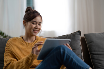Smiling millennial asian woman using modern pad gadget at home browsing Internet or shopping, happy satisfied young female client surf web read news or chat on tablet device, technology concept