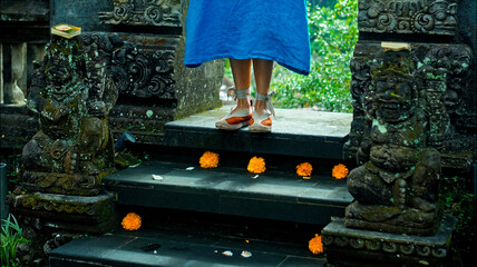 Legs of a European girl in a blue dress walking in shoes along a stone staircase with flowers