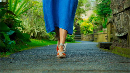 Legs of a European girl in a blue dress walking in shoes along the road with antique stonework