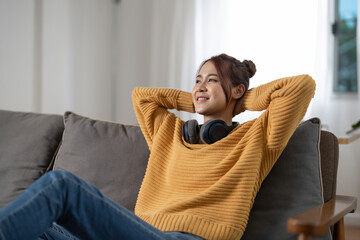 Happy smiling asian young woman in headphones listening to music lying on couch at home, people and...