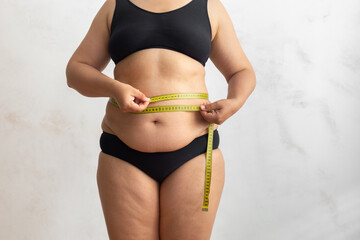 Cropped obese overweight woman with big cellulite sagging abdomen, measuring circumference of...