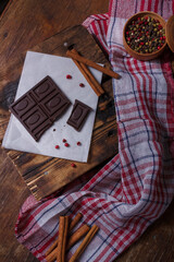 Broken bar of dark bitter chocolate with chilly pepper, red pea pepper, cinnamon flavour on paper,...