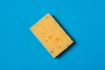 Yellow porous sponge for cleaning and washing dishes on a blue background with copy space. Homework concept.