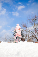 Fototapeta na wymiar Child rides on snow slide. Little girl in winter warm suit plays in fresh air and enjoys sunny day in winter, she lies in snow and plays snowballs.