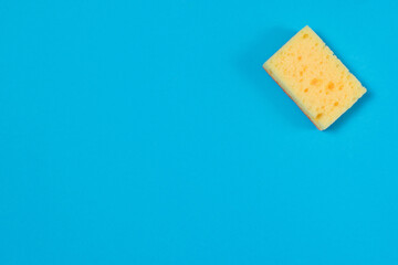 Yellow porous sponge for cleaning and washing dishes on a blue background with copy space. Homework concept.