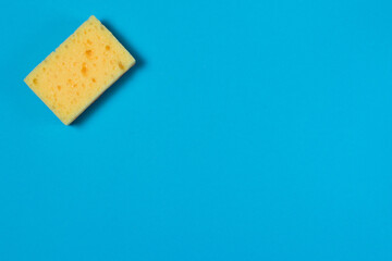Yellow porous sponge for cleaning and washing dishes on a blue background with copy space. Homework concept.
