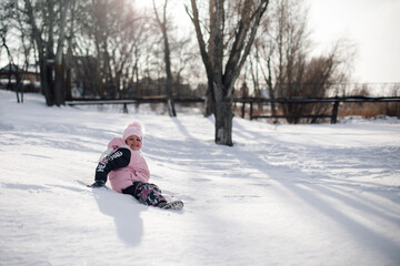 Fototapeta na wymiar Child plays in park in winter. Little girl rides snow slide and enjoys warm sunny day on winter holidays.