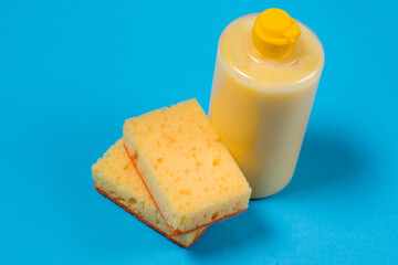 Yellow sponges for washing dishes and cleaning and liquid detergent in a transparent bottle on a blue background
