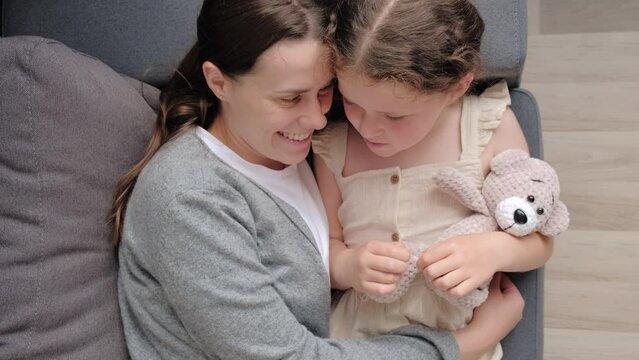 Top view of happy mother cuddles little daughter, family lying on cozy sofa touch noses feel unconditional love show devotion, express caress. Caring mom, adopted kid, Mothers Day celebration concept 