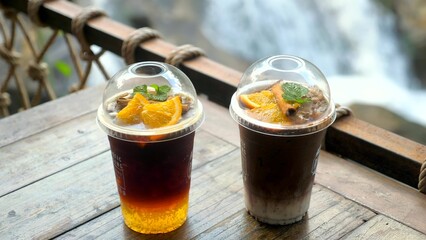 Two cups with healthy drinks in outdoor cafe. Detox cold drinks in modern cafe with waterfall view. Orange, cinnamon and mint leaf iced drinks
