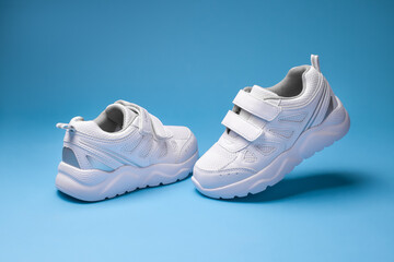 front view white child sneakers with velcro fasteners, one sneaker flying in the air and the other...