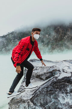 Young Man In Red Bomber Jacket Climbing A Rock At Kawah Putih Sulfer Lake